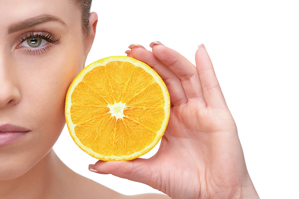 Bilde av halve ansiktet til en dame med appelsin i hånden - Nyhetsbrev: Vitamin C kan være effektivt mot oksidativt stress i kroppen